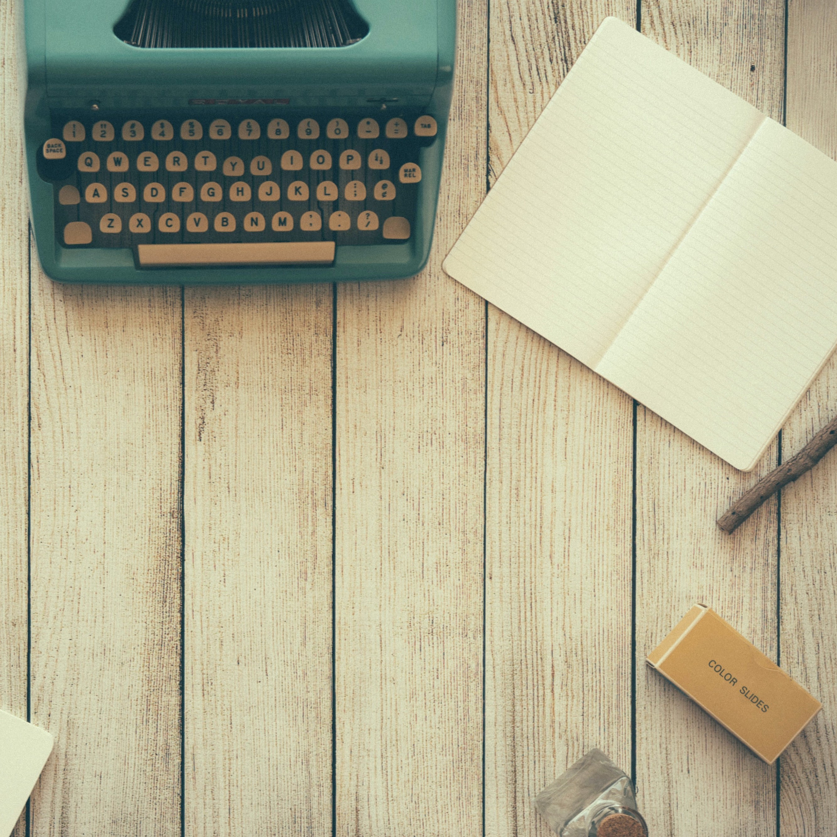 Blick von oben auf einen Tisch, darauf eine Schreibmaschine, ein Notizblock und ein Stift